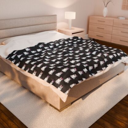 Cute ghosts in a white sheet wearing pink and purple bows on velveteen blanket.