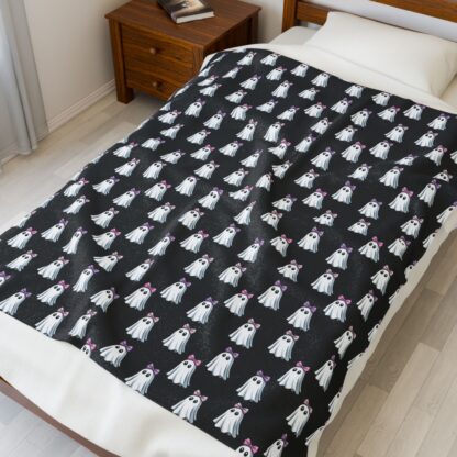 Cute ghosts in a white sheet wearing pink and purple bows on velveteen blanket.